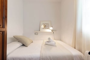 Una cama bien hecha con una toalla enrollada, una lámpara de noche y un cuadro en un estante sobre la cama.