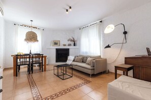 Una sala de estar con sofá, una mesa de comedor con sillas, una mesita de centro, chimenea y lámpara.