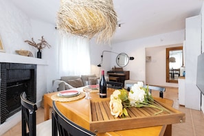 A dining area with a wooden table, chairs, a wine bottle, and a vase of flowers.