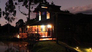 Eine zweistöckige Holzhütte mit großen Fenstern, einer Terrasse und einem kleinen Pool.