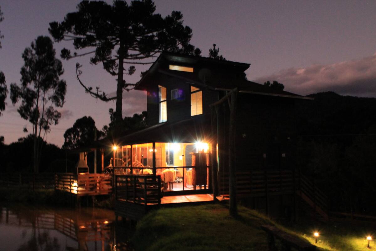 Eine zweistöckige Holzhütte mit großen Fenstern, einer Terrasse und einem kleinen Pool.