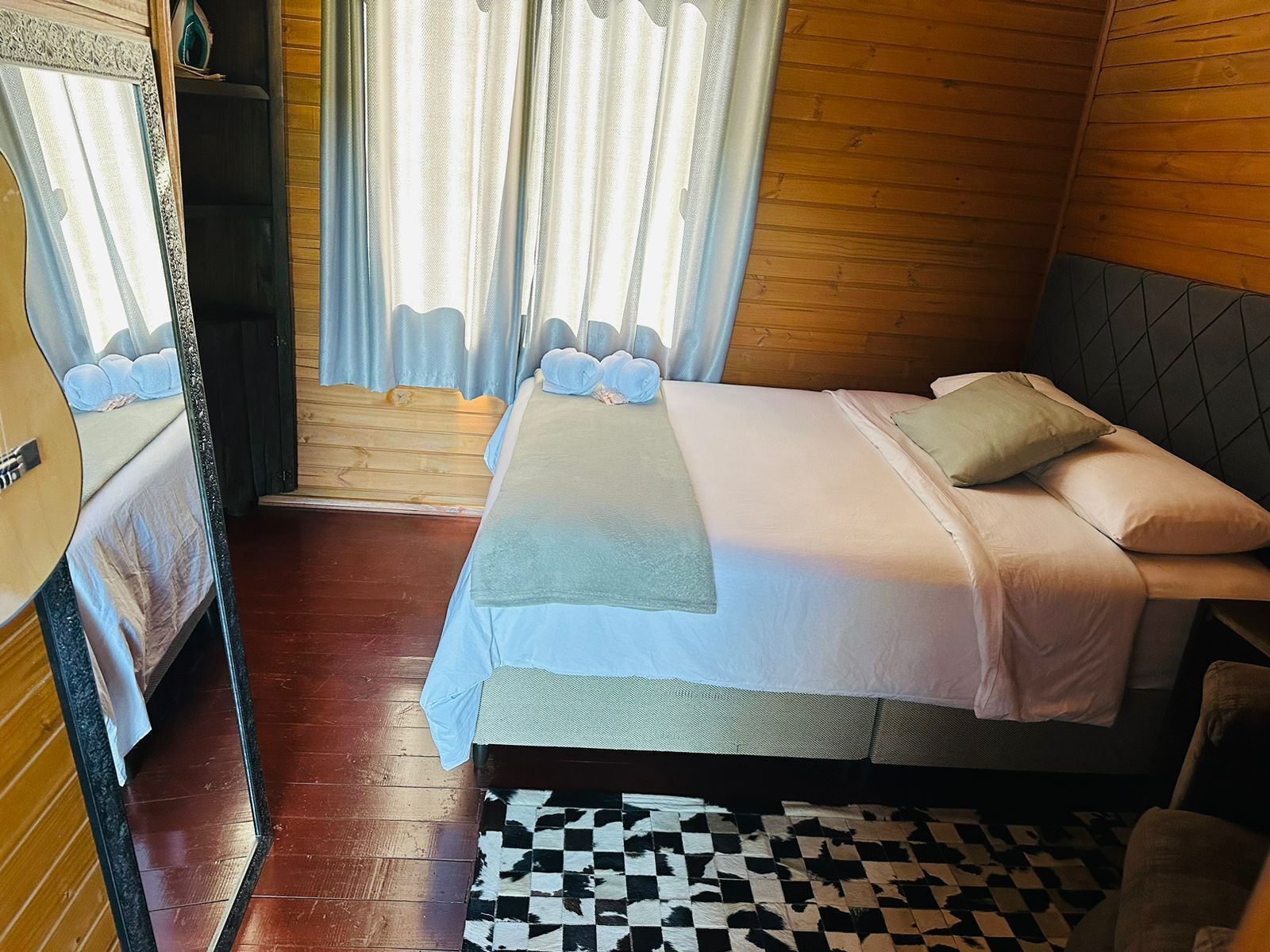 A bedroom with a bed, a checkered rug, wooden walls, and a window with curtains.
