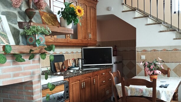 Une cuisine avec des meubles de rangement en bois, une cheminée en briques, une table à manger avec des chaises et un escalier.