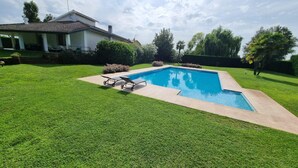 A rectangular swimming pool with a tiled deck, surrounded by well-maintained grass and a few bushes. - Villa Savalin, a refined residence nestled in the quiet of Taglio di Po (Taglio di Po)