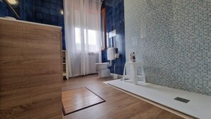 A bathroom with a wooden floor, a white sink, a toilet, and a shower area with a tiled wall. - Villa Savalin, a refined residence nestled in the quiet of Taglio di Po (Taglio di Po)