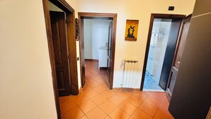 A corridor with tiled flooring, a radiator, and a door leading to another room. - Mary House (Bottai)