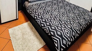 A bedroom with a bed, a white rug, and a ceiling light. - Mary House (Bottai)