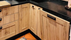 A kitchen with wooden cabinets, a black countertop, a sink, and a window with blinds. - Mary House (Bottai)