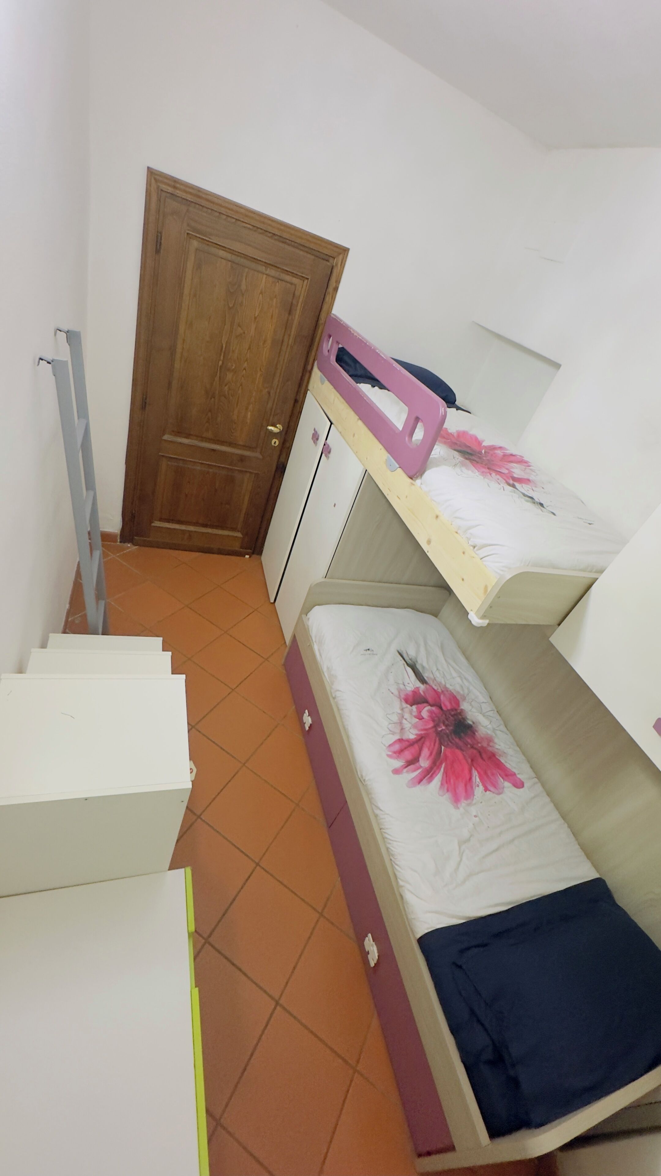 Una stanza con una porta in legno, una scala e letti a castello con biancheria da letto a fiori.