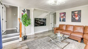 A living room with a brown leather sofa, a glass coffee table, a TV, a staircase, and a potted plant. - Walk to Harrisburg Blvd: East Downtown Houston Apt (Houston)