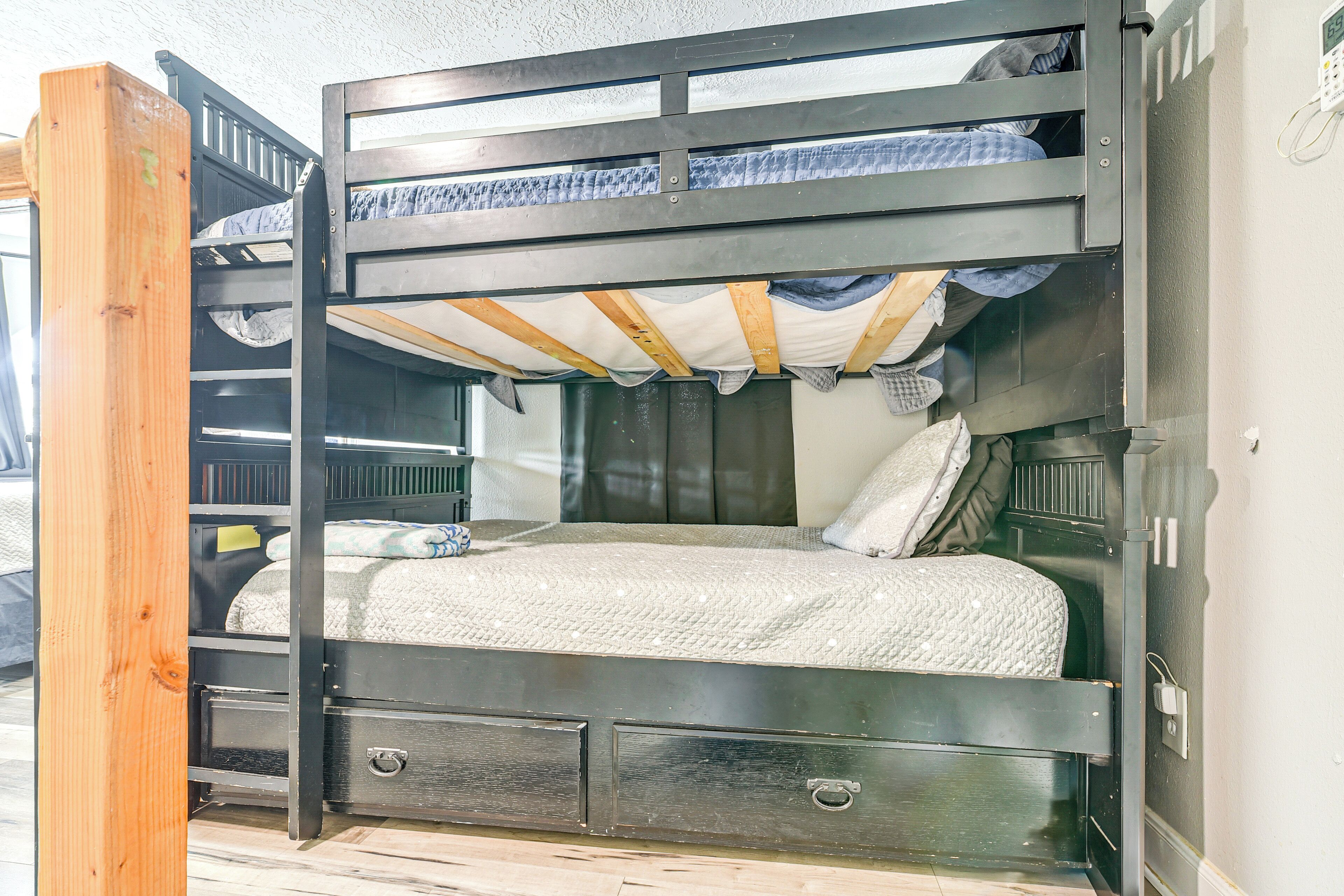 Un lit superposé avec un tiroir de rangement et un bureau escamotable, une tête de lit en bois et une fenêtre avec des rideaux.