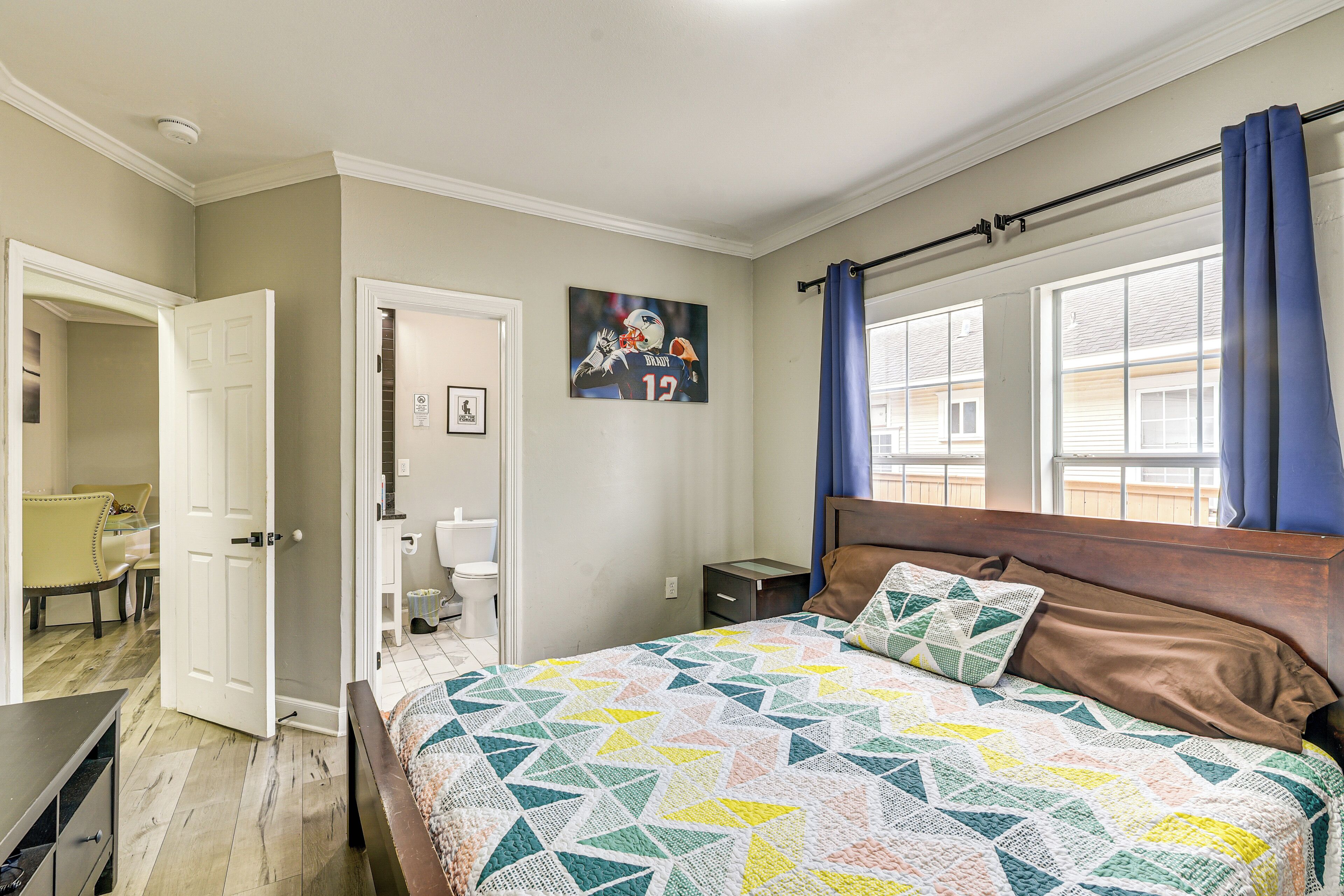 Un dormitorio con cama, mesita de noche, silla, puerta y ventana con cortinas.