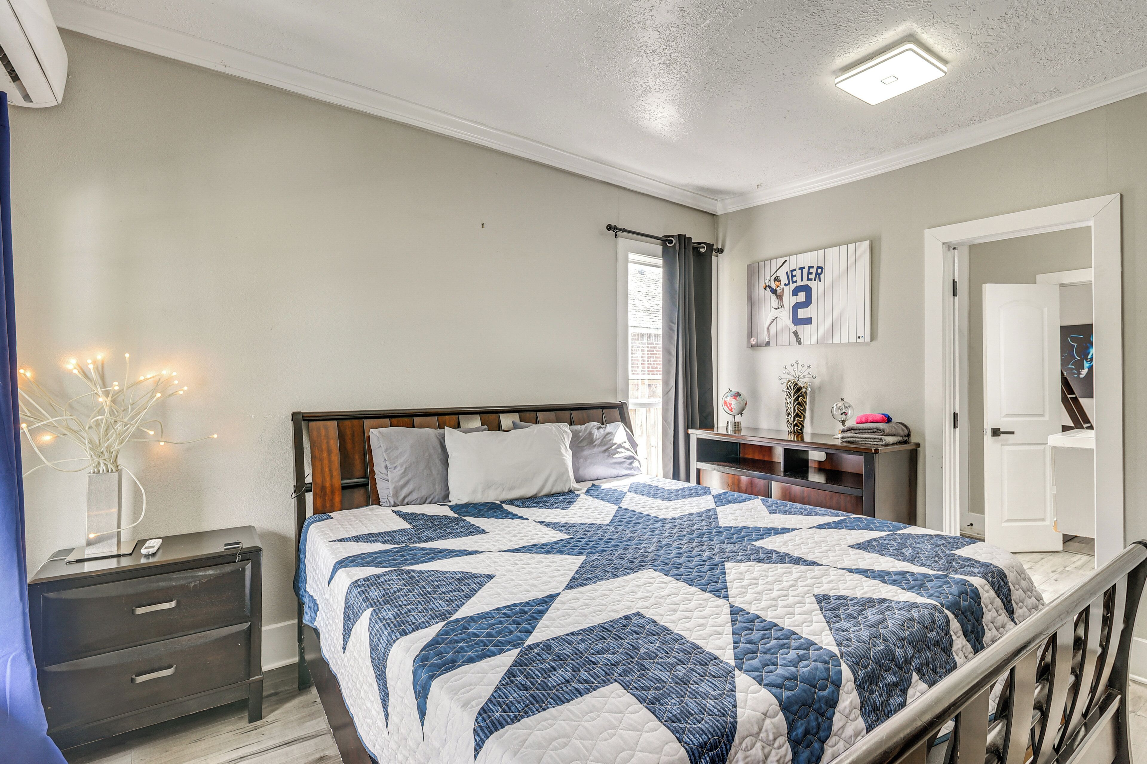 A bedroom with a bed, a nightstand, a dresser, a basketball jersey on the wall, and a door leading to another room.