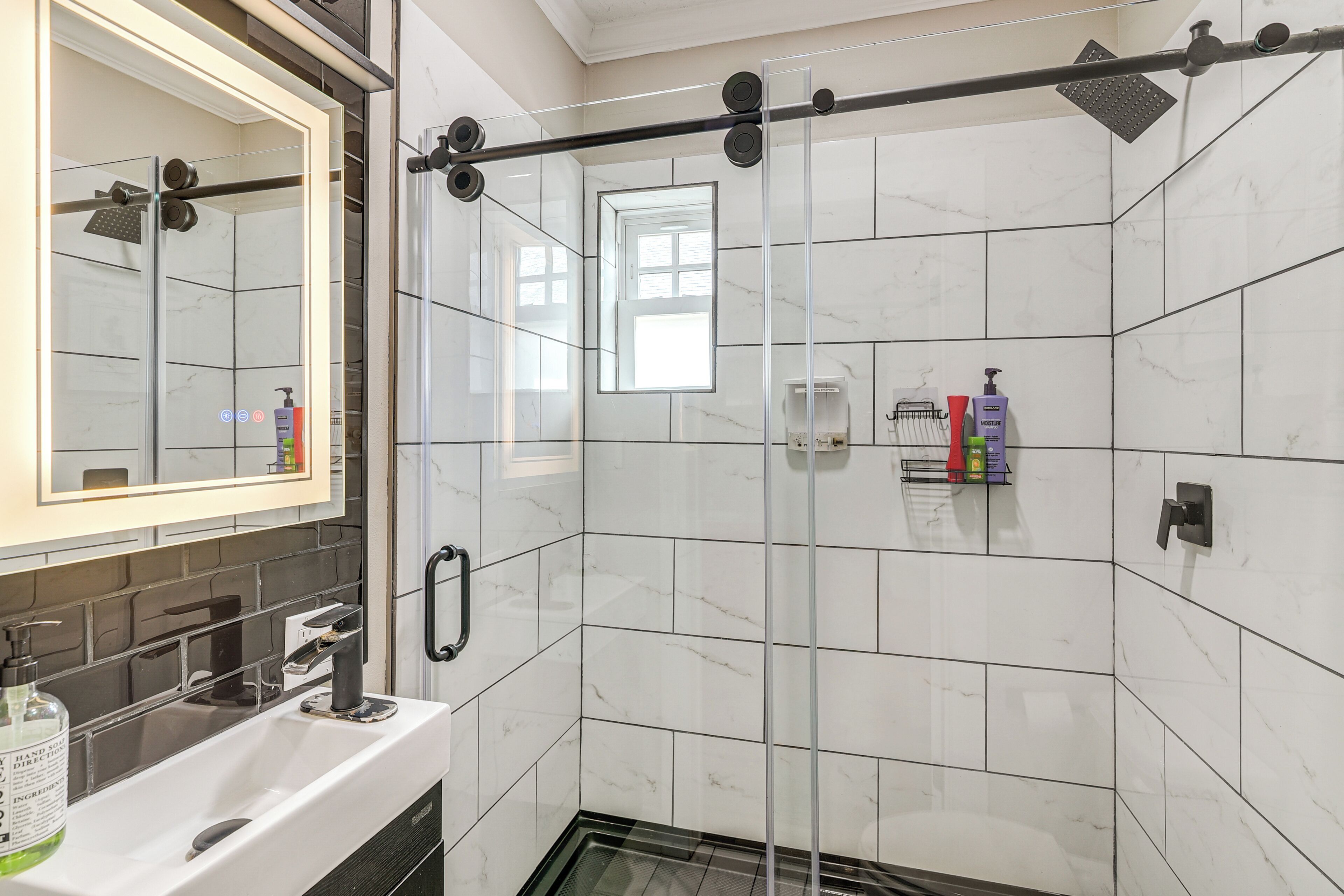 A modern bathroom with a glass-enclosed shower, a white sink with a mirror, and a tiled wall.