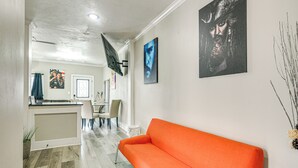 Un interior moderno con un sofá naranja brillante, una zona de cocina y obras de arte en las paredes.