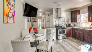 Una cocina moderna con electrodomésticos de acero inoxidable, un comedor con mesa de vidrio y un televisor montado en la pared.