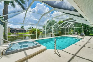 Une piscine couverte avec un jacuzzi, entourée d’une structure métallique blanche, donnant sur un espace paysager agrémenté de palmiers et offrant une vue sur un bâtiment en arrière-plan.