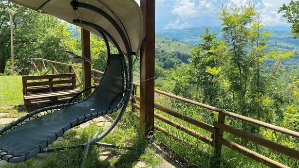 Un espacio de estar al aire libre cubierto con una hamaca, un banco de madera y vistas a un paisaje montañoso.