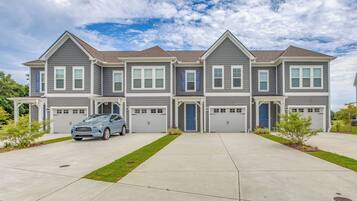 A multi-story residential building with a garage, a driveway, and a blue car parked in front.