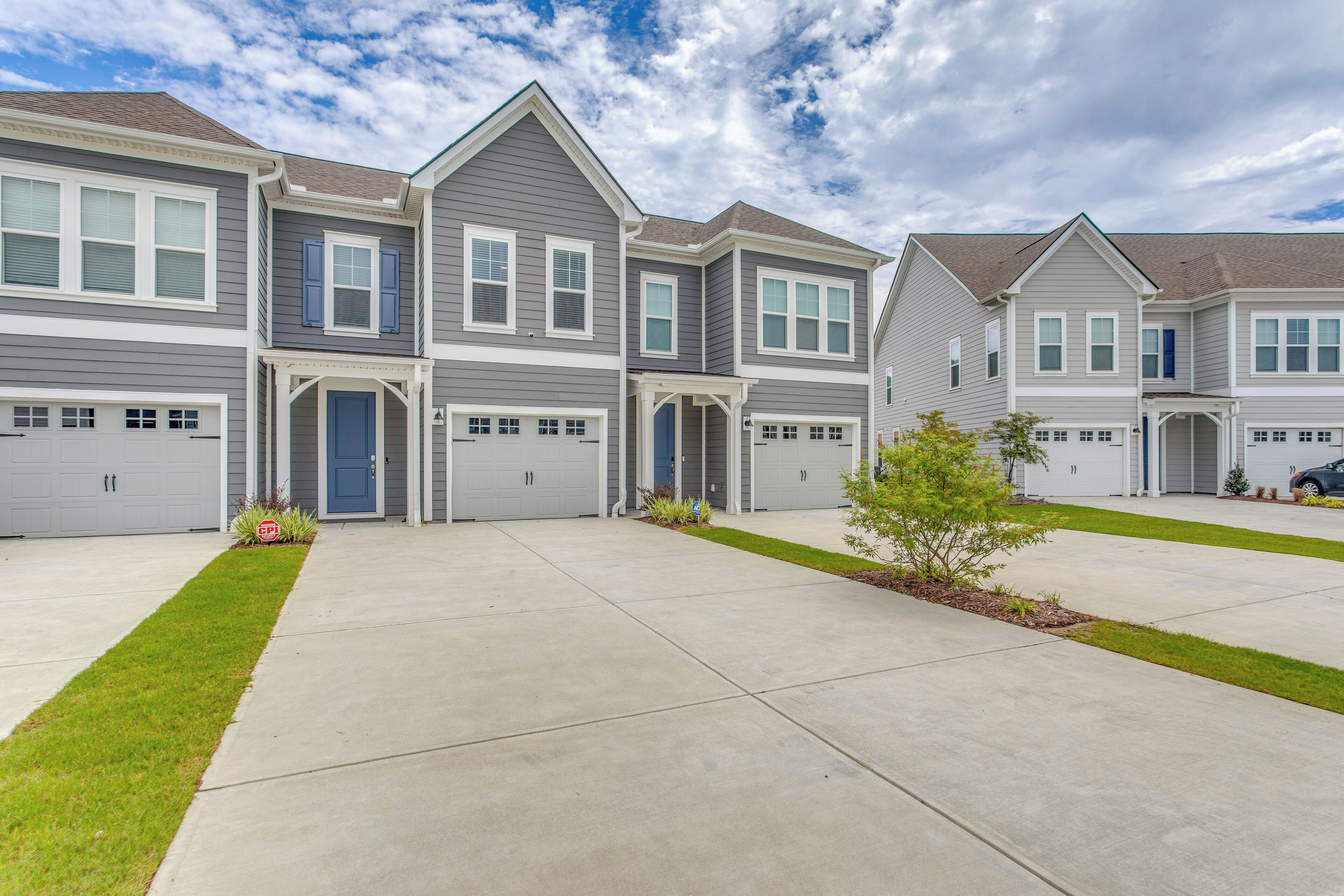 A row of two-story townhouses with attached garages, a well-maintained lawn, and a clear sky.