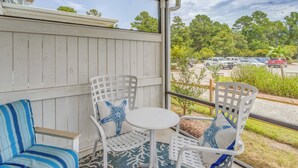 A covered outdoor seating area with white chairs and a small table, overlooking a parking lot and greenery. - Pool + Shuttle to Ocean! North Myrtle Beach Escape (North Myrtle Beach)
