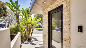 A modern building entrance with a stone facade, a glass door, and a small planter with green plants. - Shop, Dine & Walk to Ocean: Redondo Beach Apt! (Redondo Beach)