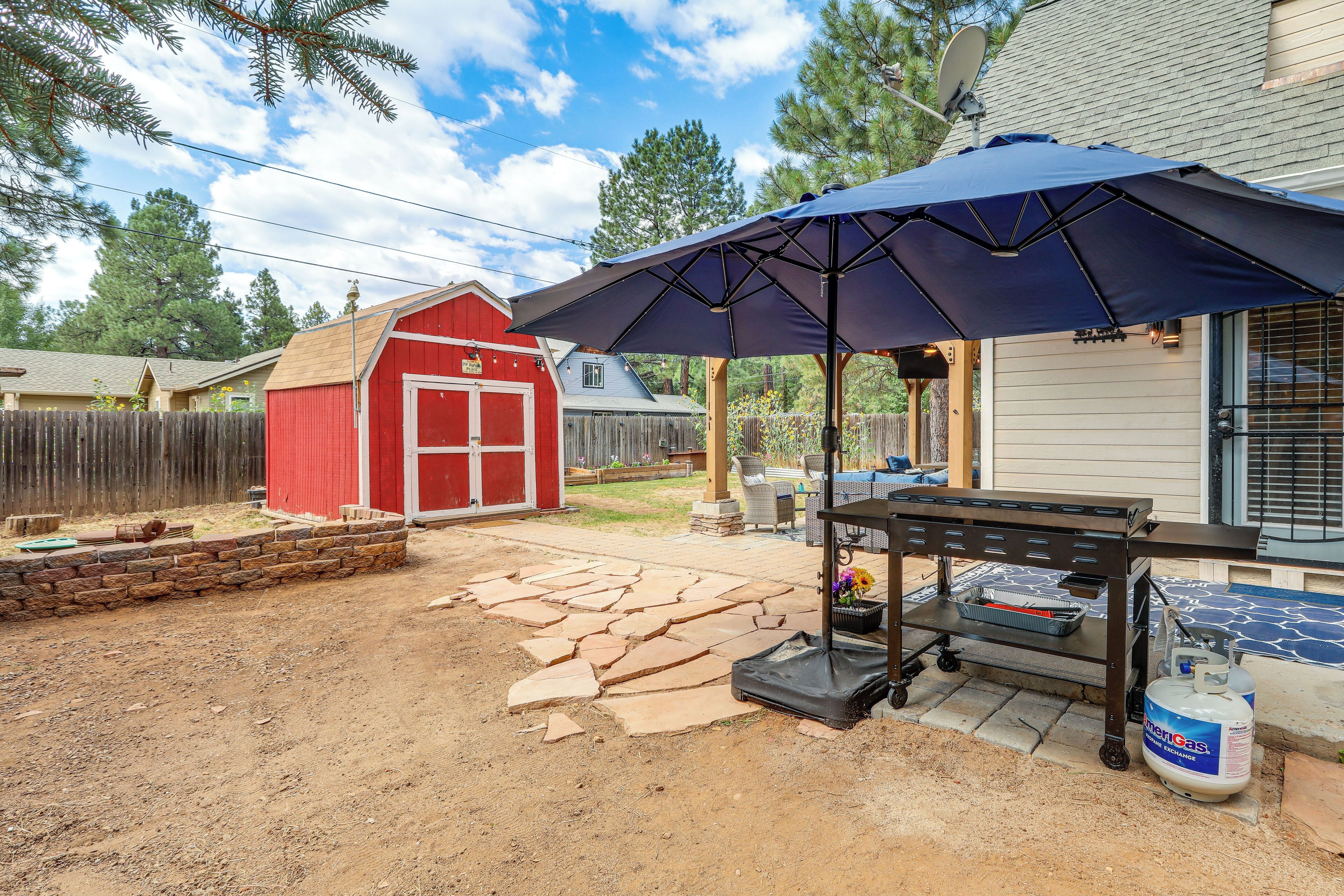 Ein Garten mit einer roten Gerätehütte, einer Terrasse mit Steinplatten und einem Gasbehälter.