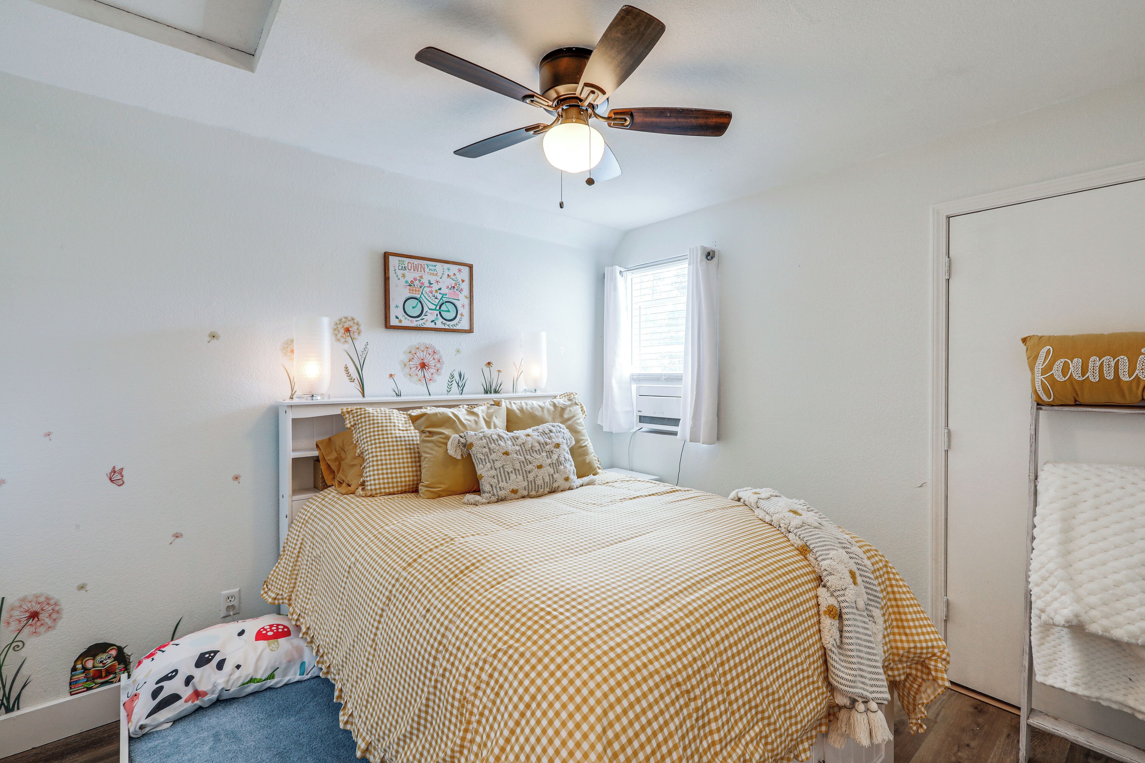 A bedroom with a bed, a ceiling fan, a window, and a wall-mounted shelf with decorative items.