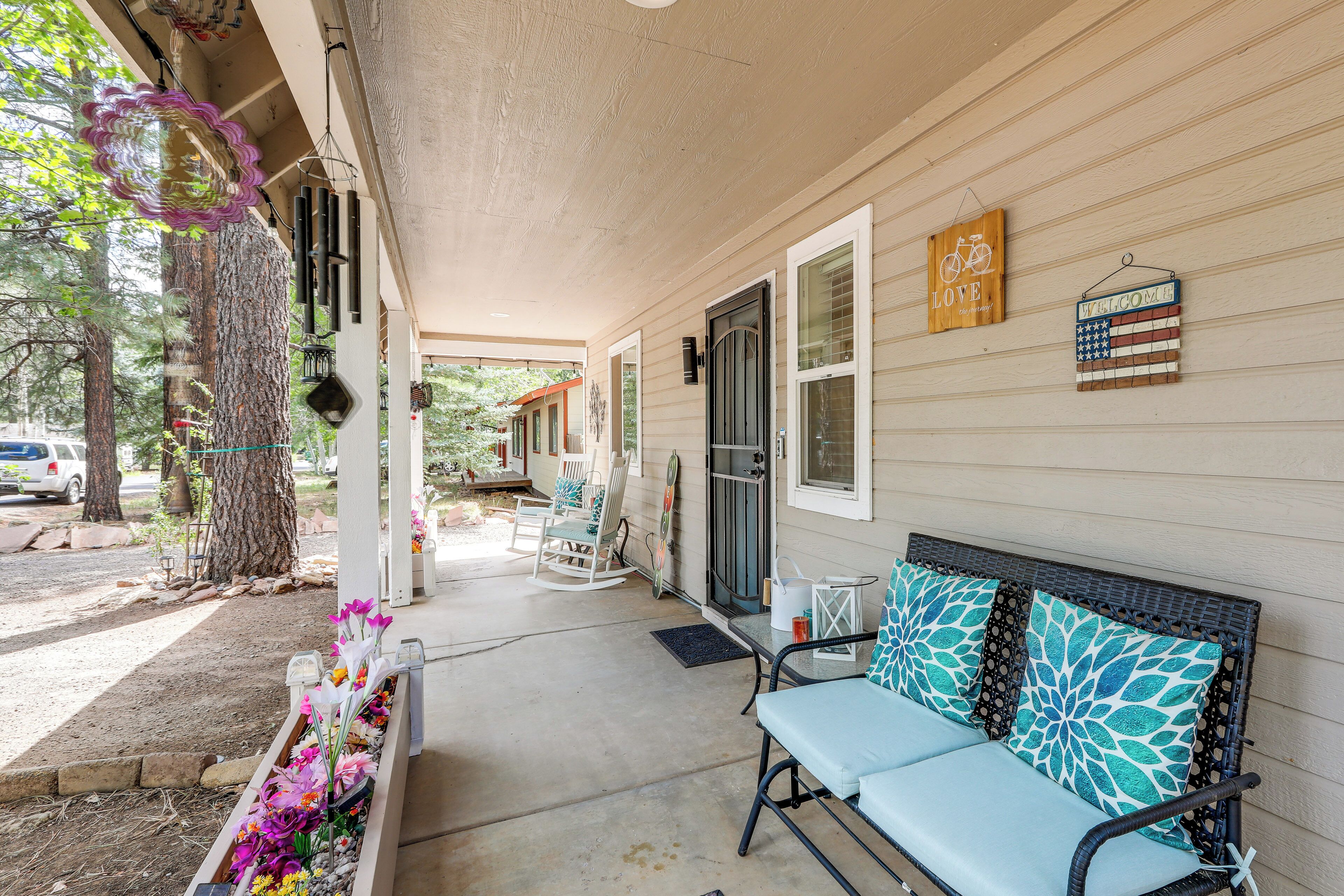 A covered porch with a bench, chairs, and a flower planter.