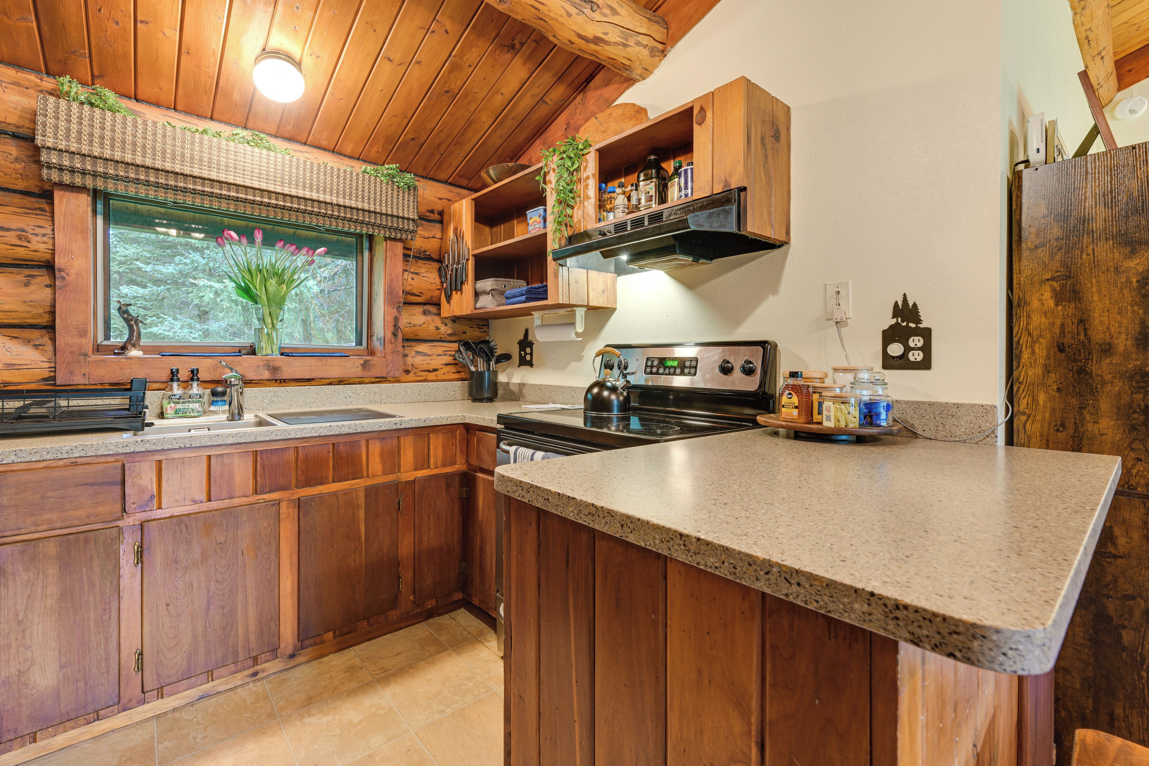 Une cuisine avec des meubles en bois, un plan de travail en granit, une cuisinière et une fenêtre donnant sur les arbres.