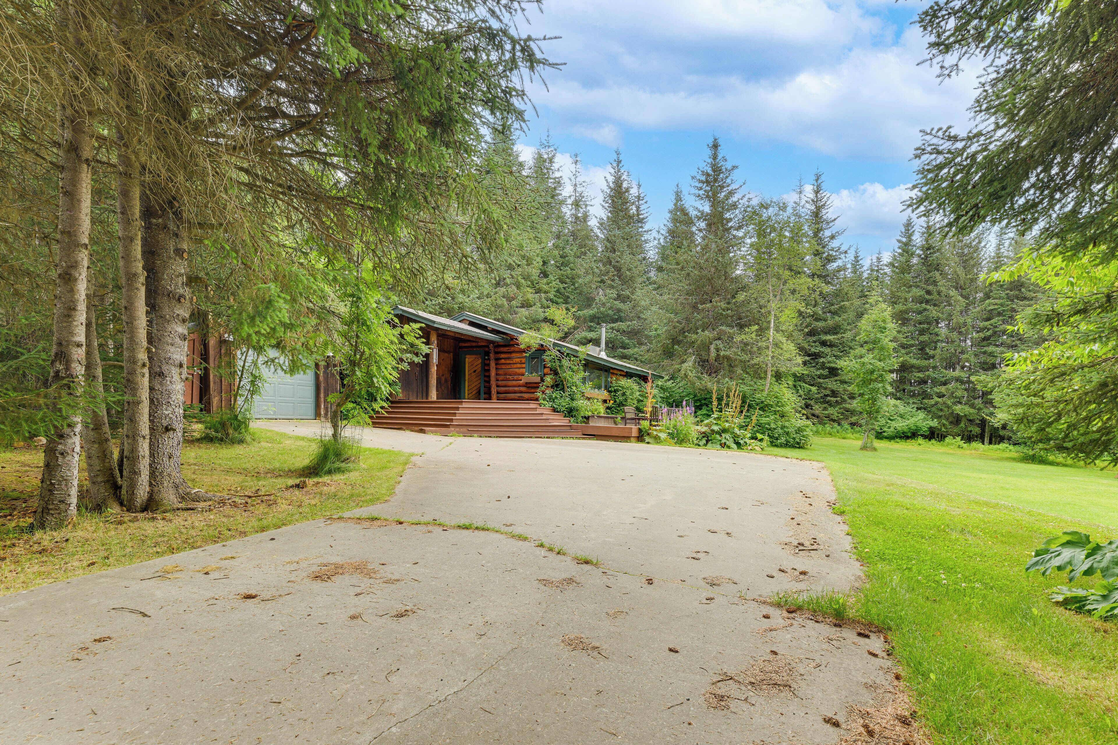 A log cabin with a concrete path leading to the entrance, surrounded by dense forest.