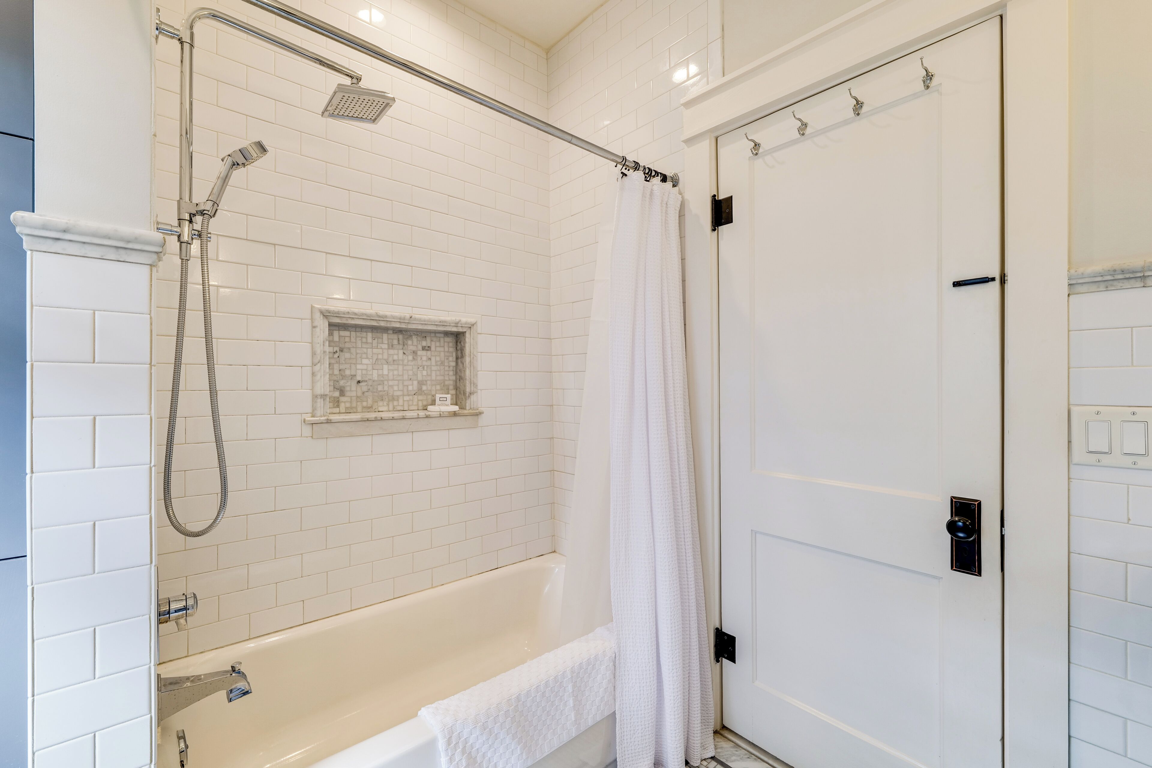 A modern bathroom with a bathtub, shower, and white tiled walls.