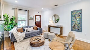 Een moderne woonkamer met een grijze bank, poefs, een salontafel en een schilderij aan de muur.
