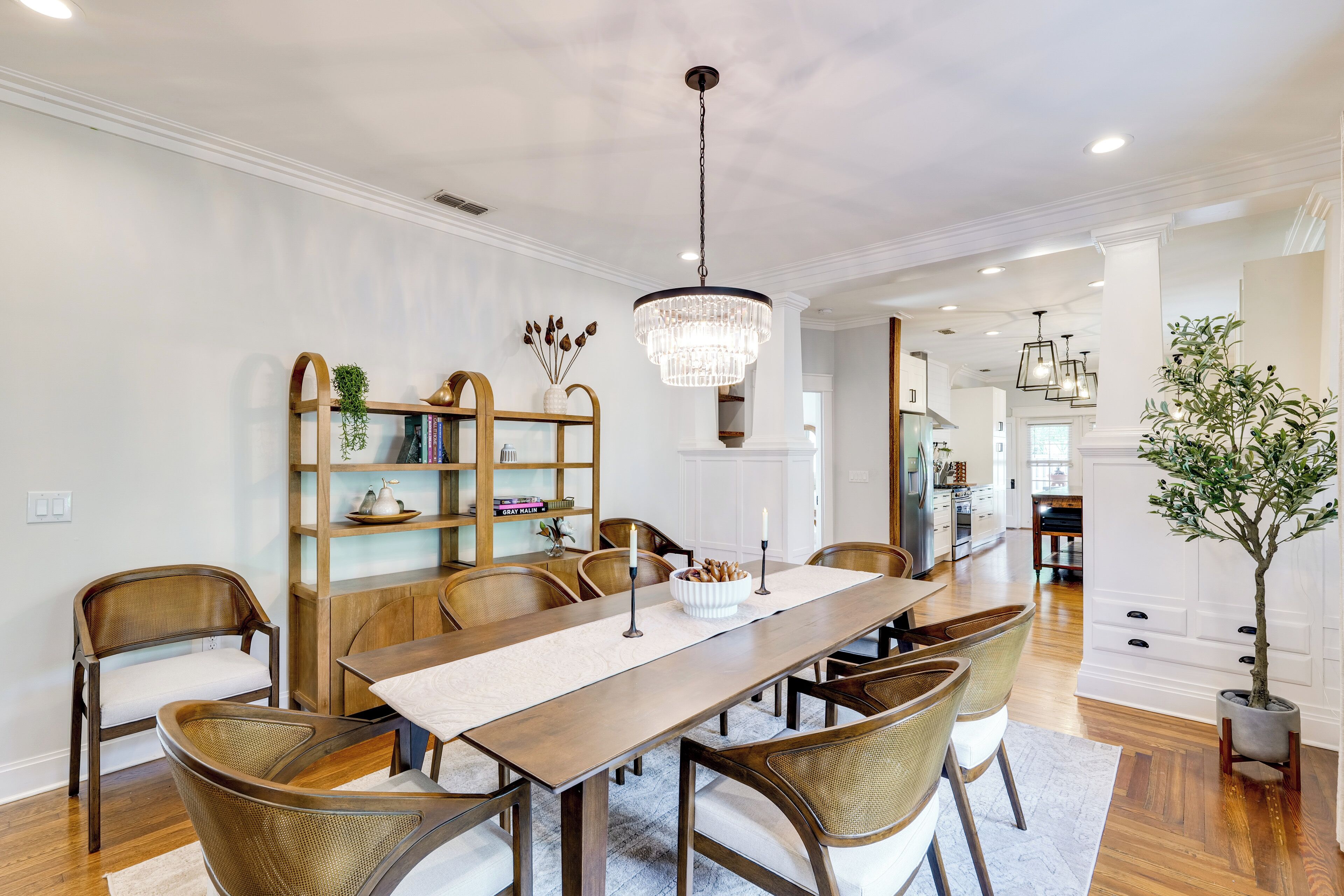 A dining room with a wooden table, wicker chairs, a chandelier, and a bookshelf.