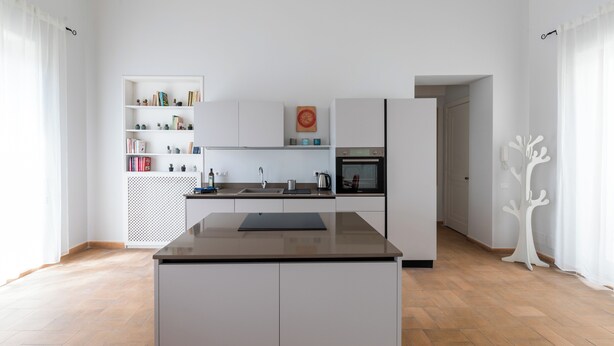 A modern kitchen with white cabinetry, a central island, and a built-in bookshelf.