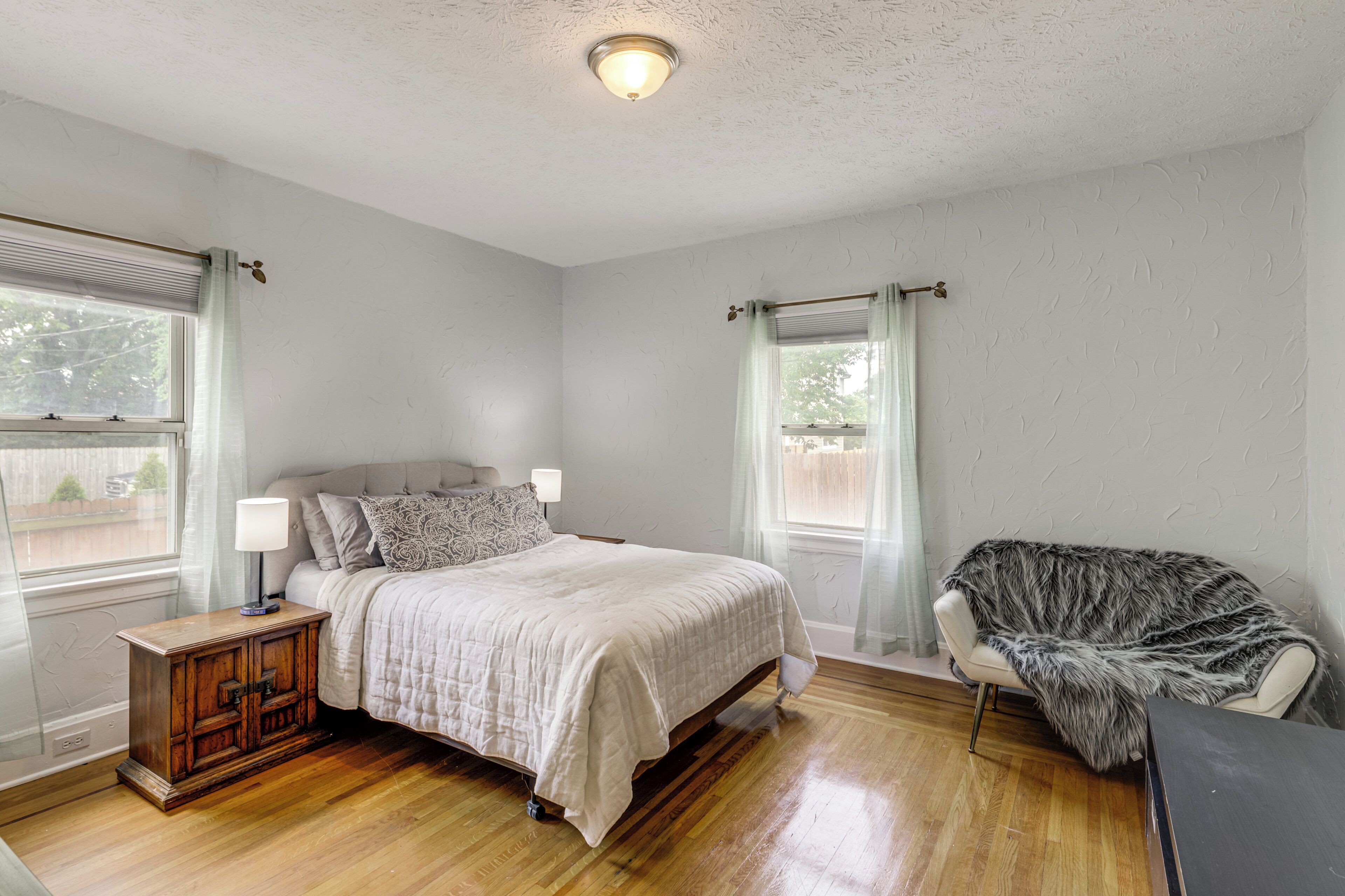 Un dormitorio con cama, mesitas de noche, una silla y una ventana.