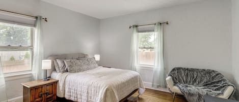 Un dormitorio con cama, mesitas de noche, una silla y una ventana.