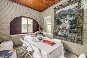 A dining area with a brick wall, a large framed painting, and a table set with white tablecloths and chairs. - Modern Group Getaway w/ Private Yard in Cincinnati (Cincinnati)