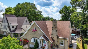Une maison d’habitation avec une façade en briques, un porche à l’avant et une cour arrière comprenant une terrasse et du mobilier d’extérieur.