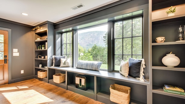 Ein modernes Interieur mit einer eingebauten Bank an einem großen Fenster, Regalen mit dekorativen Gegenständen und Holzboden.