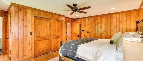 Un dormitorio con paredes de madera, una cama con ropa blanca, un ventilador de techo y una lámpara de noche.
