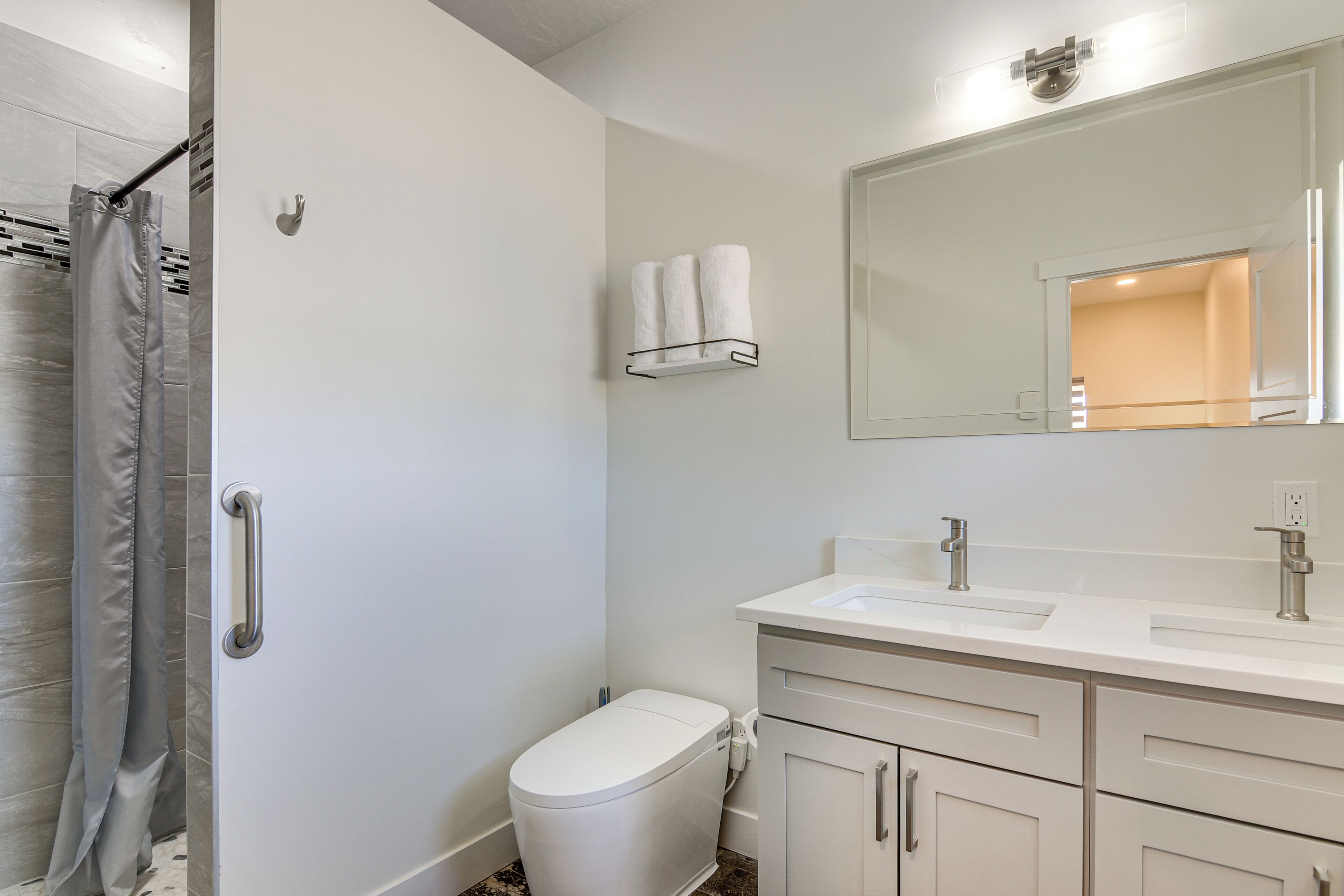 A bathroom with a toilet, sink, mirror, and towel rack.