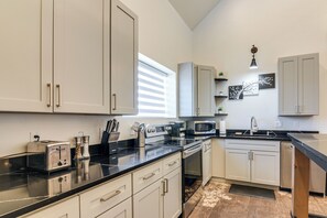 A modern kitchen with white cabinets, a black countertop, stainless steel appliances, and a window with blinds. - Between Bryce Canyon & Zion: Hiker's Paradise! (Hatch)