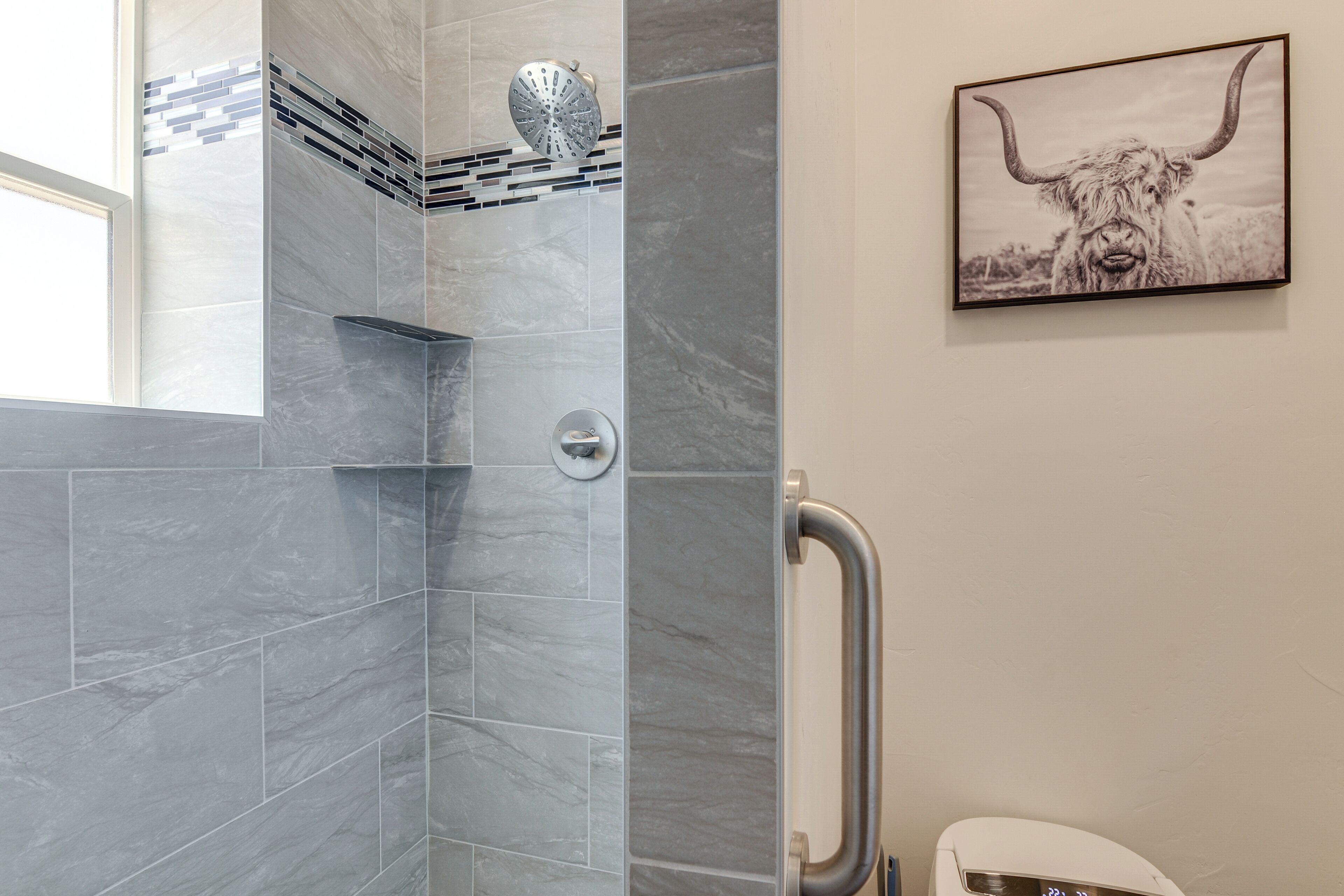 A bathroom with grey marble tiles, a shower with a rain showerhead, a toilet with a digital display, and a framed picture of a yak on the wall.