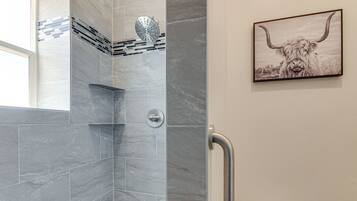 Un baño con baldosas de mármol gris, ducha con cabezal de lluvia, inodoro con pantalla digital y un cuadro enmarcado de un yak en la pared.