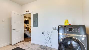 A laundry room with a front-loading washing machine, a door to a staircase, and a wall-mounted electrical box.
