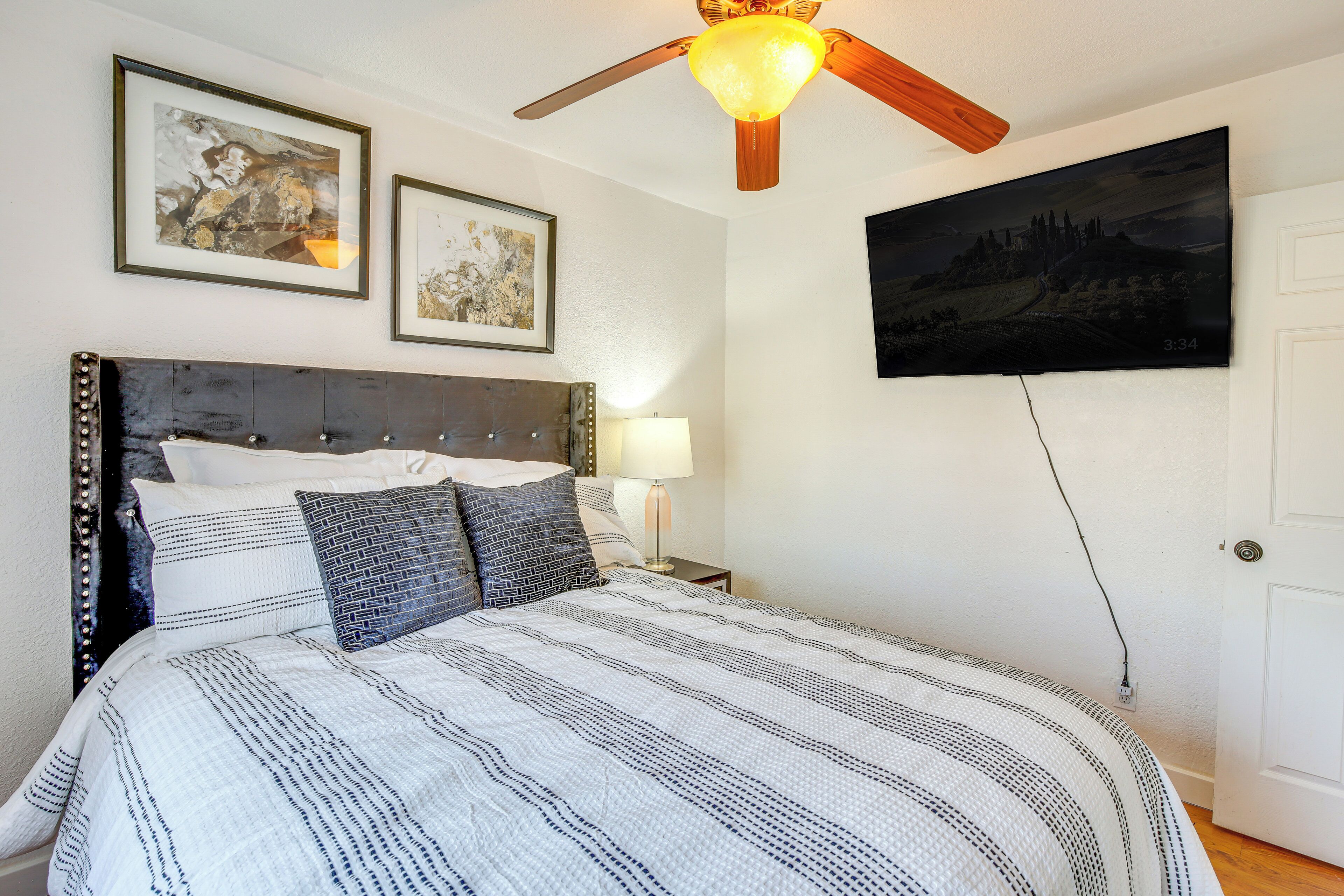 Une chambre à coucher avec un lit, un ventilateur de plafond, deux tableaux encadrés et un téléviseur fixé au mur.