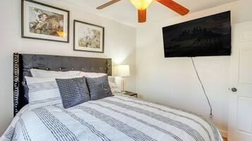 Une chambre à coucher avec un lit, un ventilateur de plafond, deux tableaux encadrés et un téléviseur fixé au mur.