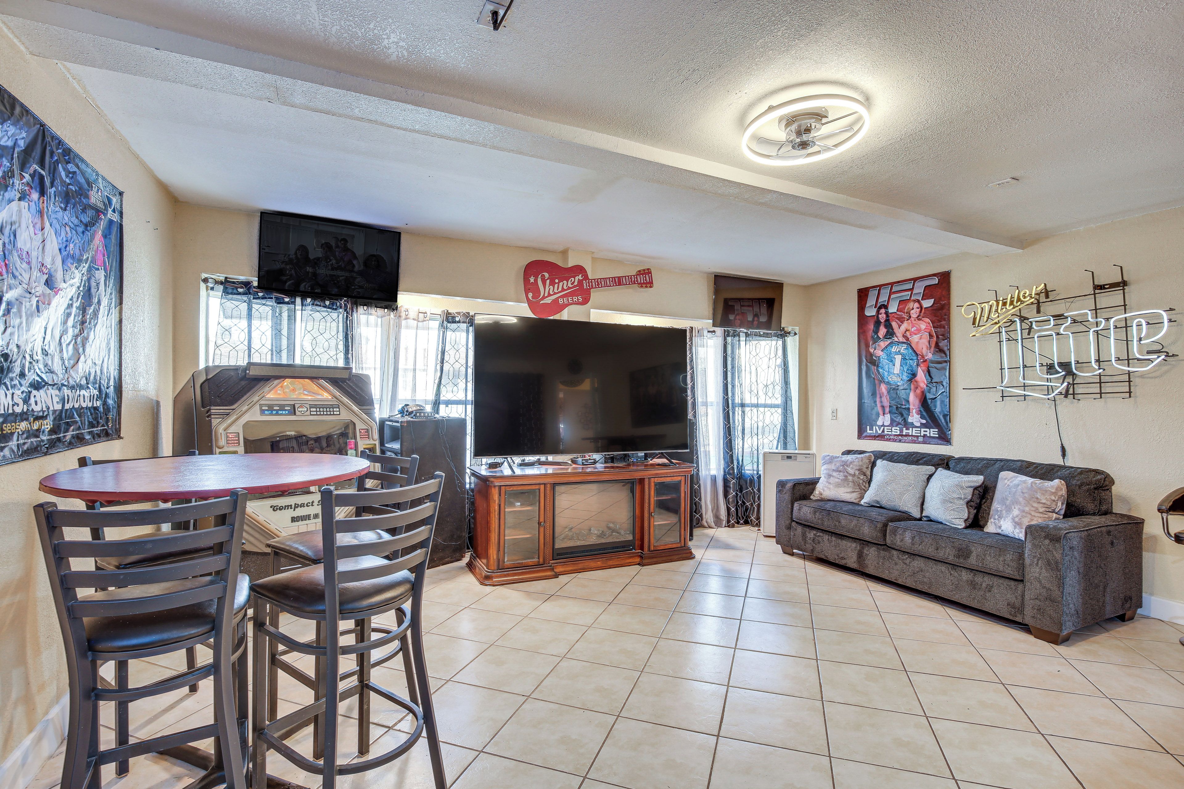 Una sala de estar con televisor, sofá, mesa de centro y una zona de bar con taburetes.