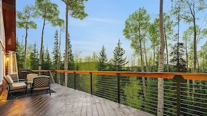 A wooden deck with outdoor furniture, surrounded by a railing and overlooking a forested area. - Hot Tub, Game Room! 3-story Brian Head Home (Brian Head)